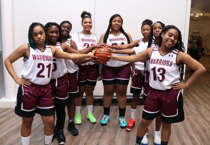 Members of the girls basketball team, standing in a V shape with all players holding a basketball.